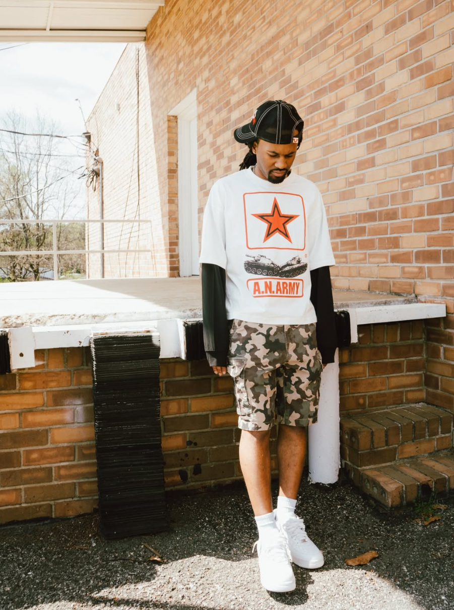 Model wearing A.N. Army double layered long-sleeve with camo shorts, brick wall backdrop
